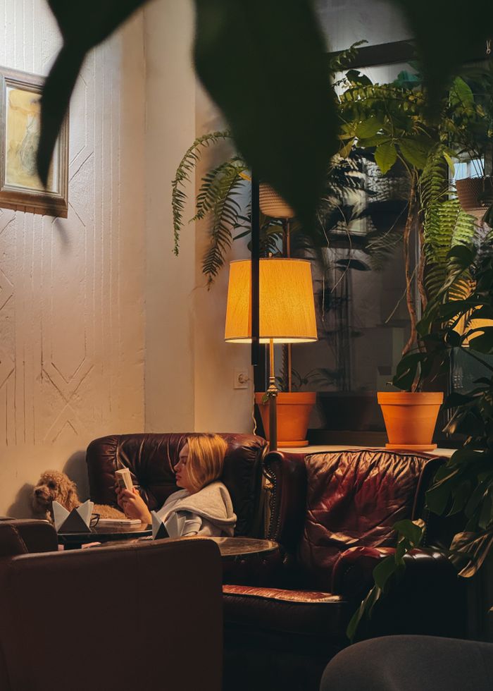 about-01 A woman relaxing with her pet in a cozy indoor reading area, surrounded by green plants and warm lighting.